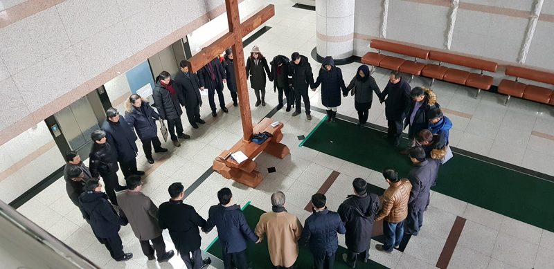 실내 십자가를 가운데 두고 손을 맞잡아 둥글게 선 동문들